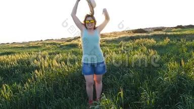 戴帽子的快乐年轻女子在夕阳下的绿野中享受夏日
